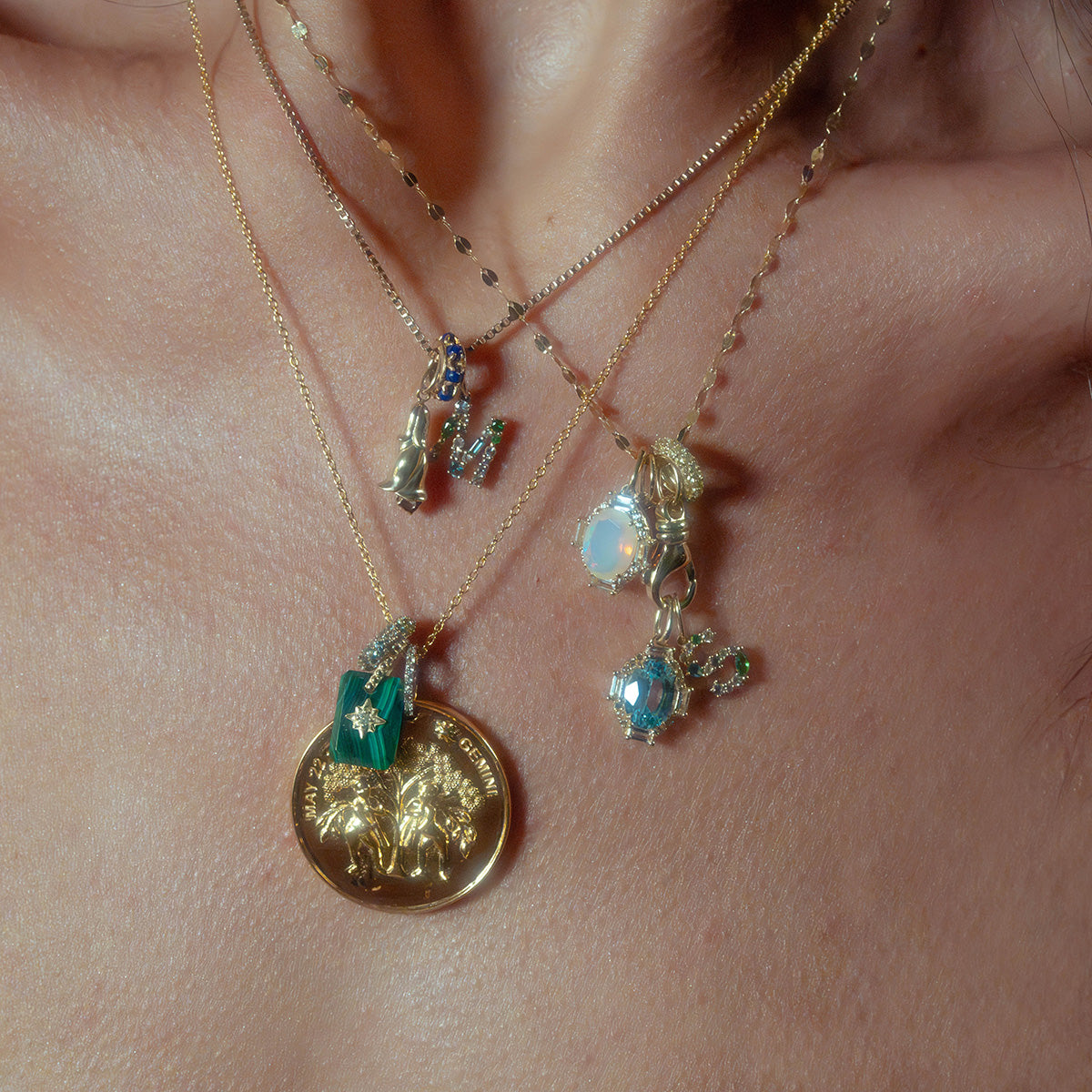 Close-up of a neck adorned with layered gold necklaces, featuring the Solid Gold Vintage Inspired Birthstone Charm alongside green gemstone, opal, and blue gem pendants, all elegantly styled against bare skin.