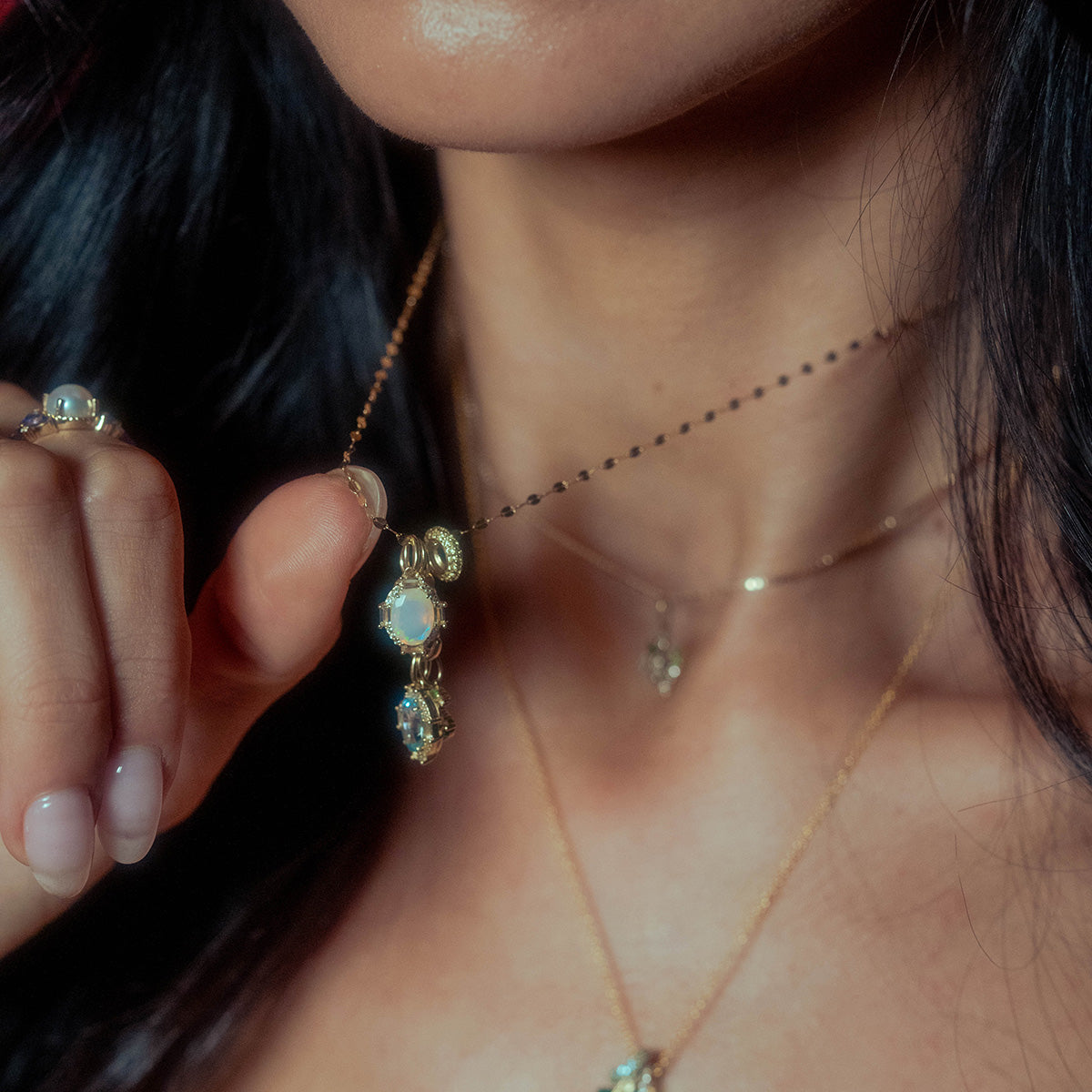 A close-up of a woman holding the Solid Gold Vintage Inspired Birthstone Charm, displaying her manicured nails along with part of her face, lips, and dark hair.