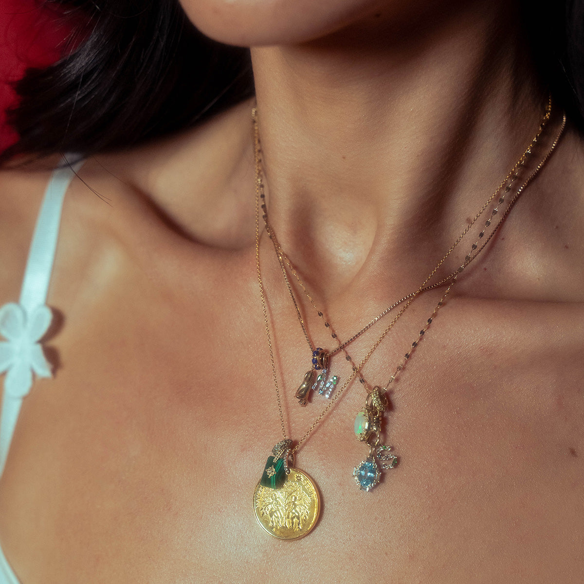 A close-up of a womans neck adorned with layered gold vermeil necklaces, including the Vintage Inspired Zodiac Coin Necklace. She wears a white top featuring a floral strap detail.