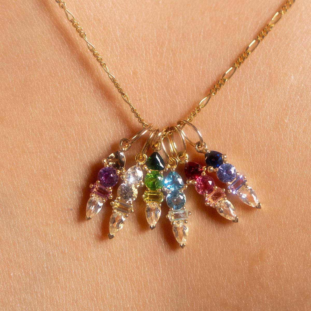 The Solid Gold Modern Ombre Birthstone Charm necklace features five crystal pendants, each accented with a unique gemstone color—purple, green, blue, pink, and dark blue—for a graceful and modern accessory.
