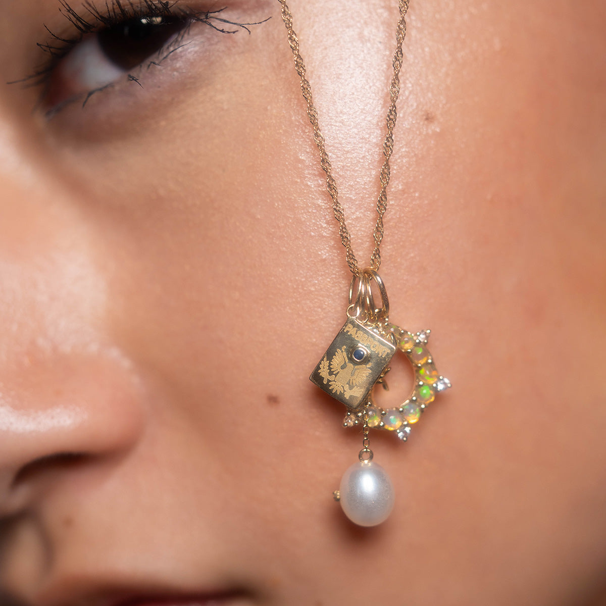 Close-up of a persons face wearing the Solid Gold Statement Charm necklace in 9k yellow gold, featuring a square engraved charm, an iridescent crescent, and a dangling pearl, showcasing smooth skin and intricate solid gold details.
