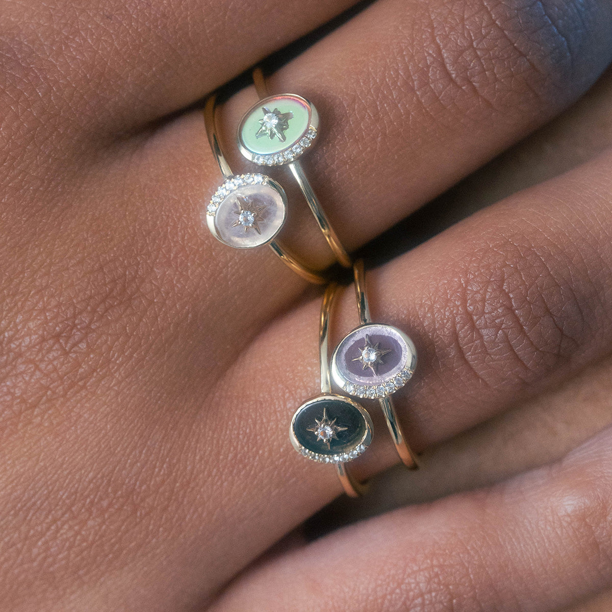A Solid Gold Crystal Crescent Moon Ring for Manifestation with an oval, pastel gemstone setting and a central star design is worn on a finger with medium brown skin.