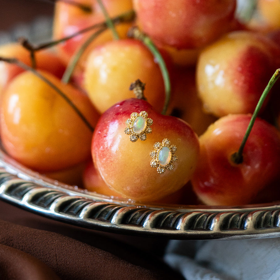 A close-up of yellow and red cherries on a silver plate, with one cherry in front adorned with the Opal Majesty Studs.