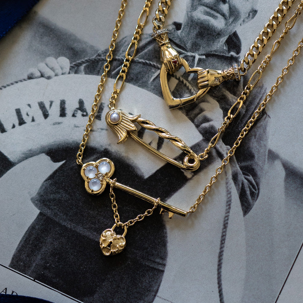 The Lock and Key Necklace, along with three other vintage romance necklaces—a heart, a horseshoe with pearls, and a pin with a pearl—is displayed on a black-and-white photo of someone holding a sign.