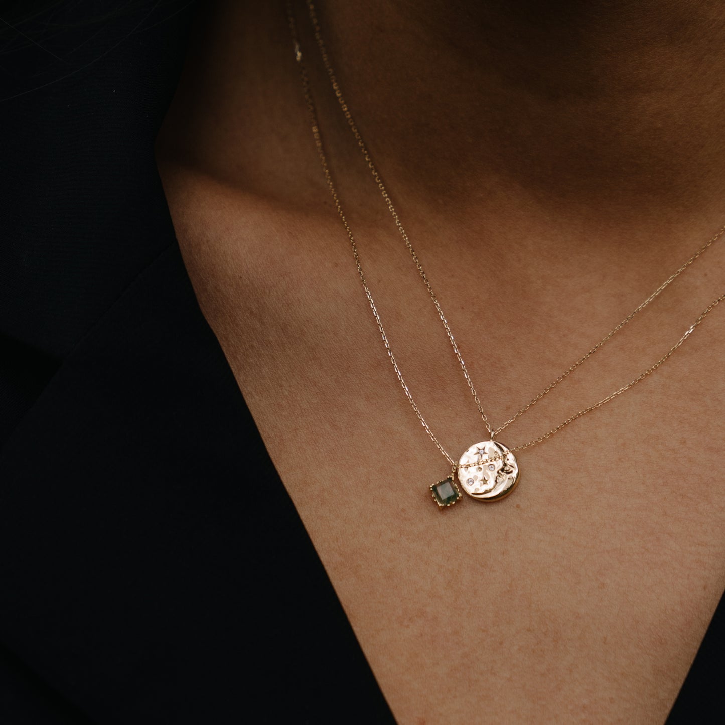 A close-up shows a person in a dark top wearing two delicate solid gold necklaces: one is the Solid Gold Aquatic Agate Necklace for Grounding with a small green gemstone pendant, the other features a round gold textured pendant.