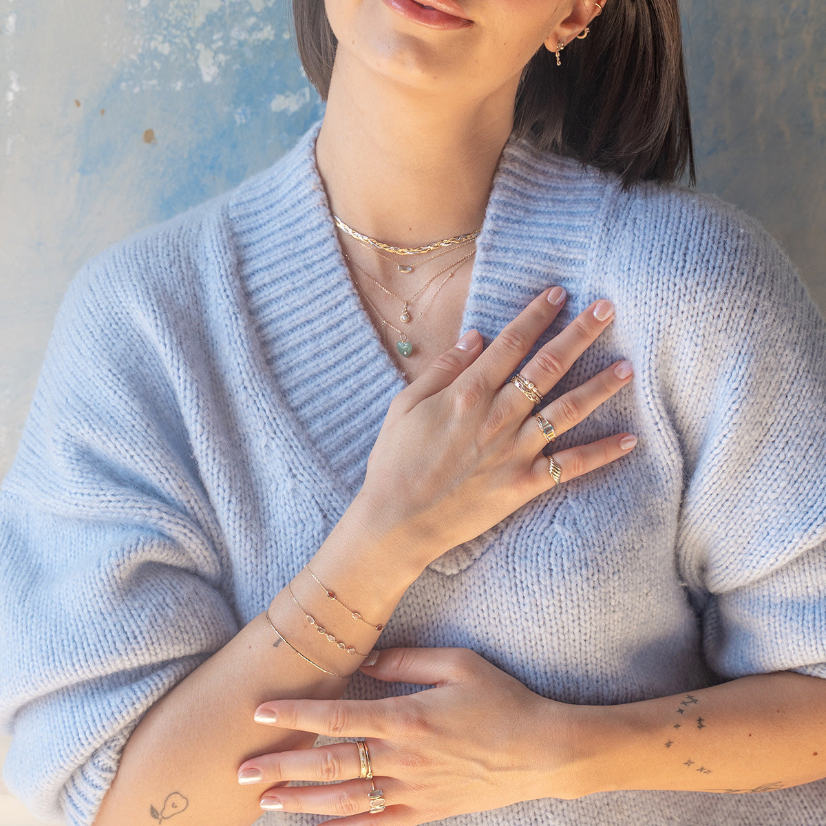 A woman in a sweater gently rests her hand on her chest, highlighting the Solid Gold Daybreak Moonstone and Blue Topaz Bracelet.