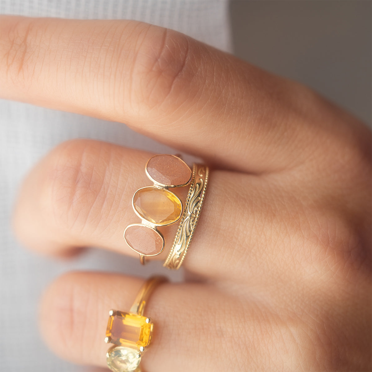A close-up of a hand wearing two vintage gold rings—one with three oval yellow stones, one engraved—and the Solid Gold Filigree Ring with a large rectangular yellow gemstone on the index finger.