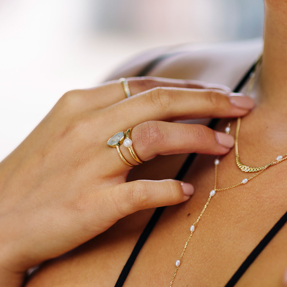 A close-up of a womans hand wearing the Solid Gold Bold Pearl Ring Sample, featuring manicured nails and a black strappy top.