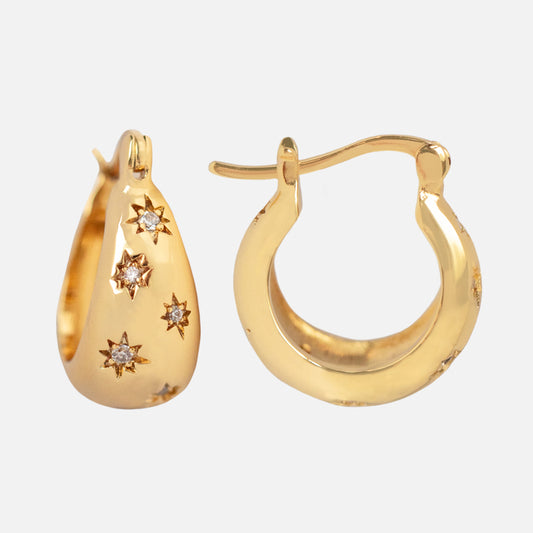 The Cosmic Tapered Huggie Earrings feature 14k yellow gold plating with star-shaped engravings and central diamonds for a touch of cosmic elegance. Shown are two hoops: one front view, one side view.
