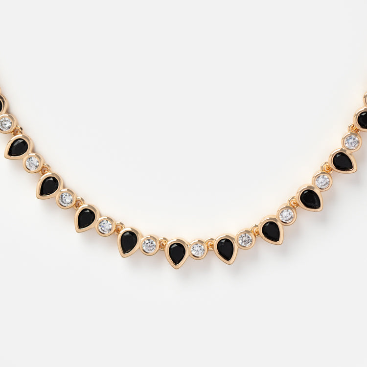 The Teardrop Tennis Necklace showcases alternating black teardrop-shaped stones and round clear cubic zirconia crystals, all set in gold and displayed on a white background.