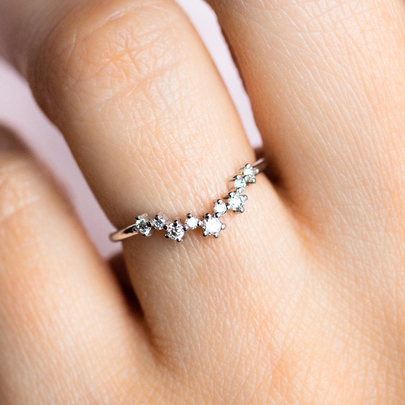 A close-up of a hand wearing the Aster Diamond Cluster Band in White Gold, sample size 4, crafted from recycled gold and set with seven ethically sourced diamonds arranged in a sparkling curve.
