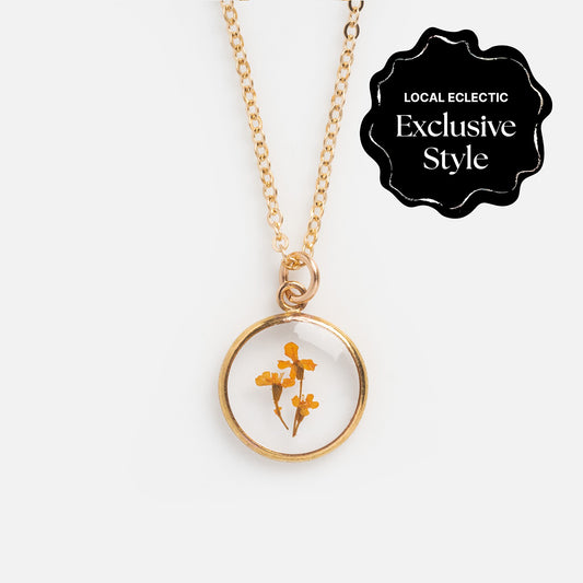 The Tiny Birth Flower Portrait Necklace features a round pendant with pressed yellow flowers in clear resin. A black label at the top right reads Local Eclectic Exclusive Style.
