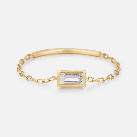 The Solid Gold White Topaz Baguette Chain Ring features a sleek gold chain with a rectangular white topaz set in a gold bezel, shown on a plain white background.