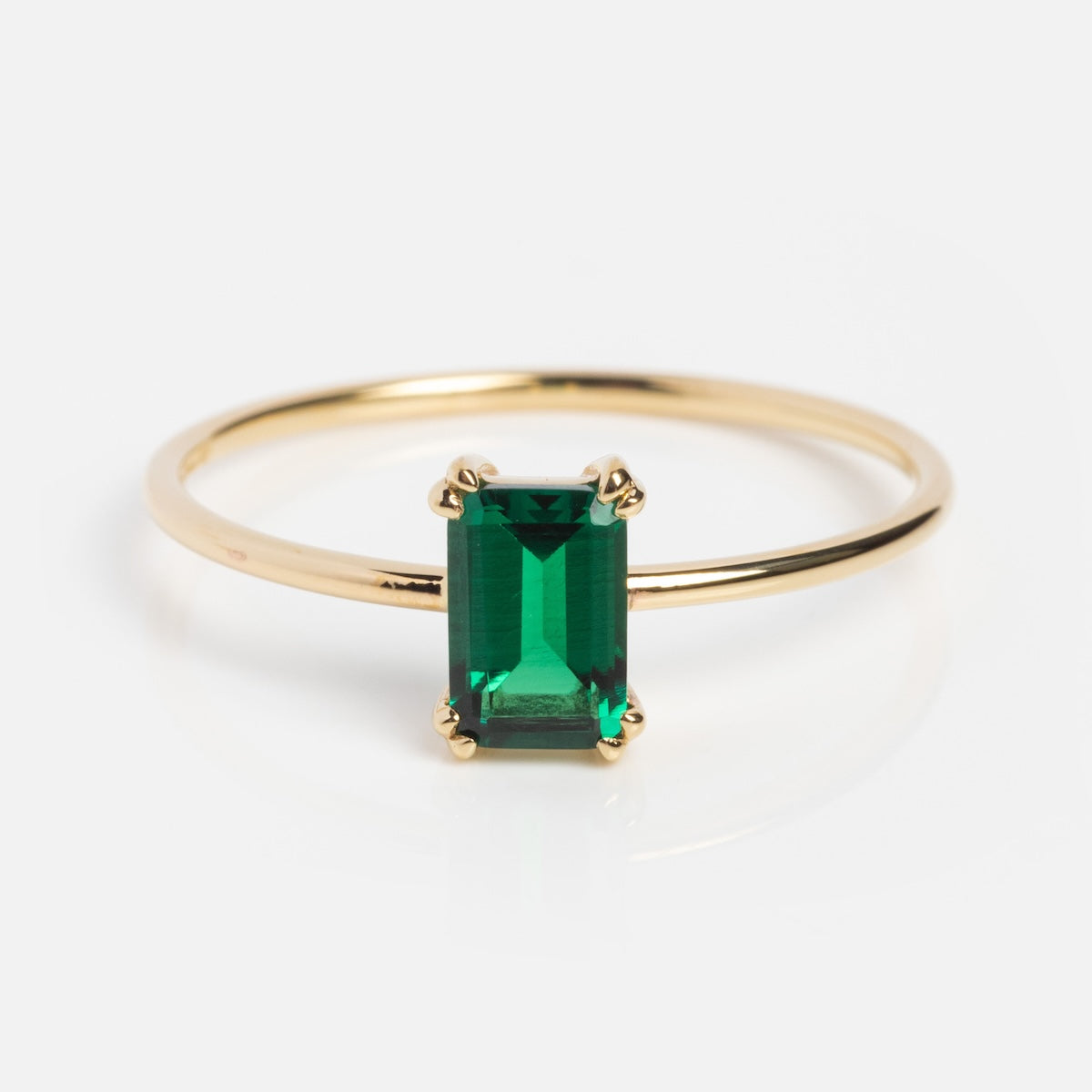 The Solid Gold Essential Baguette Birthstone Ring features a slim gold band with a rectangular green gemstone in a four-prong setting, crafted from natural stones and shown on a white background.
