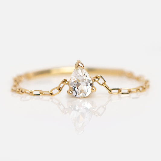 The Solid Gold White Topaz Pear Chain Ring features a clear, pear-shaped gemstone and a dainty chain band, creating an elegant look against a white backdrop.