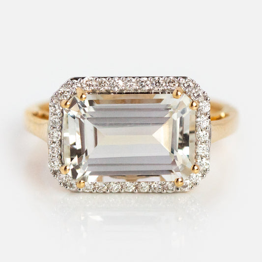 The 14k Solid Gold Diamond East West Baguette Ring features a large emerald-cut clear stone with a halo of round diamonds, displayed on a plain white background.
