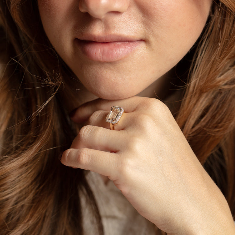 A woman with long brown hair gently touches her face, highlighting her lips, hand, and a 14k Solid Gold Diamond East West Baguette Ring sparkling elegantly on her finger.
