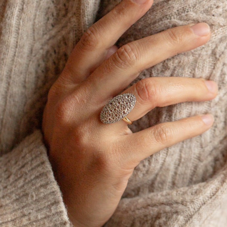 A hand wearing the 14k Solid Gold Bella Diamond Navette Ring with a modern, oval-shaped design on the middle finger, resting against a beige knitted sweater.