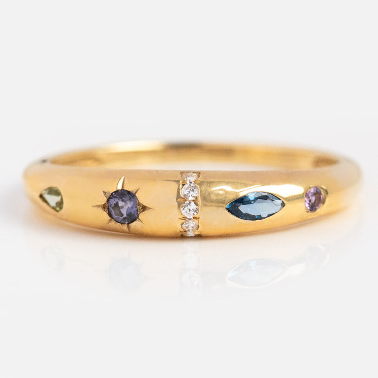 The Solid Gold Pizza Acrostic Ring features a round purple stone in a starburst setting, a marquise blue stone, rows of clear gems, and vibrant accents—capturing the playful elegance of modern acrostic jewelry.