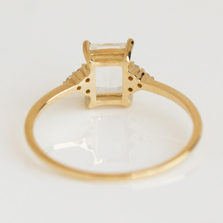 The Solid Gold Essential White Topaz Ring Sample features a rectangular clear white topaz gemstone in a raised prong setting, shown from the back on a white background.