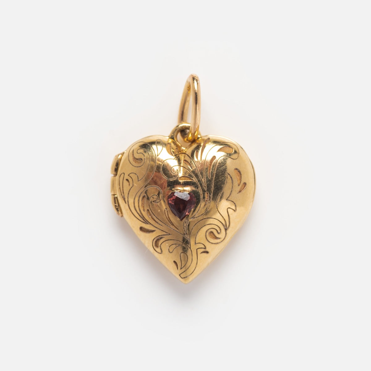 The Solid Gold Locket Charm features a heart shape with engraved swirls and a small red gemstone at its center, shown against a plain white background.