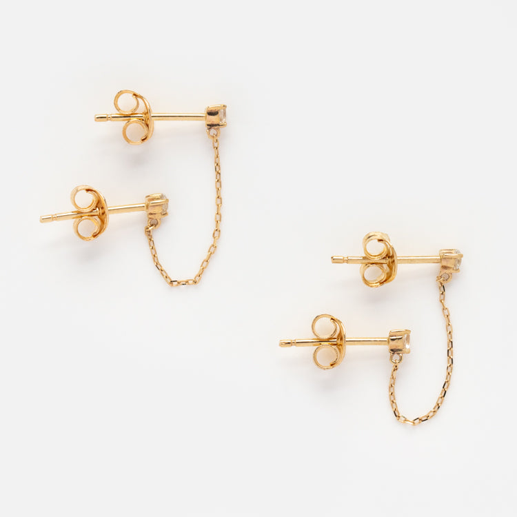 Two pairs of Solid Gold Double Piercing Chain Earrings with butterfly backs, each linked by a delicate gold chain, are displayed on a white background.