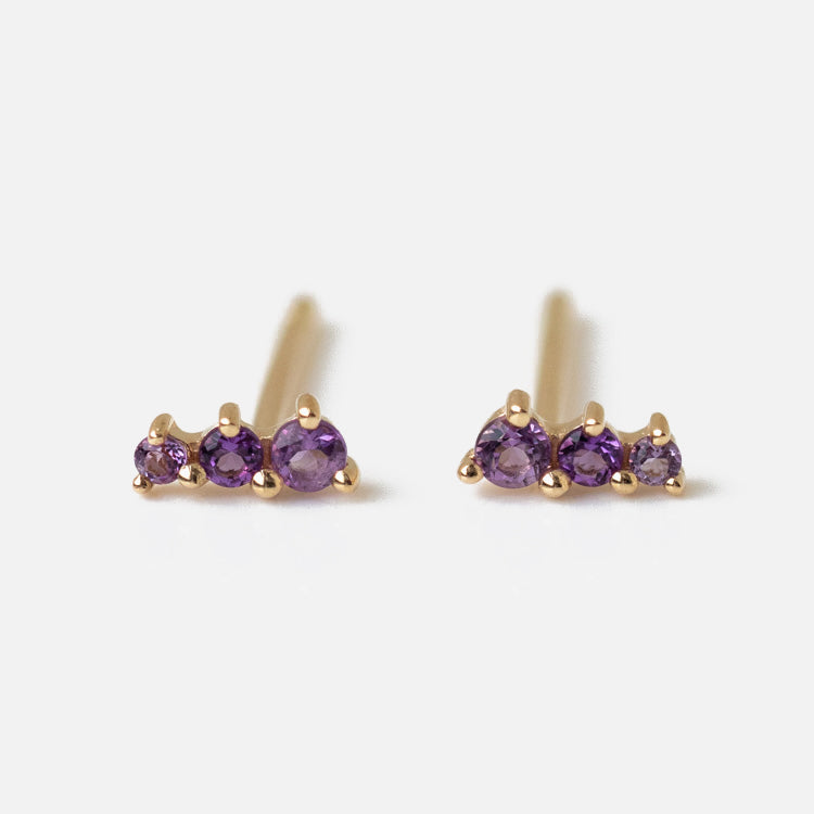 Solid Gold Dainty Birthstone Bar Studs: Minimalist studs each with three small round purple gemstones set in a row, displayed on a plain white background.