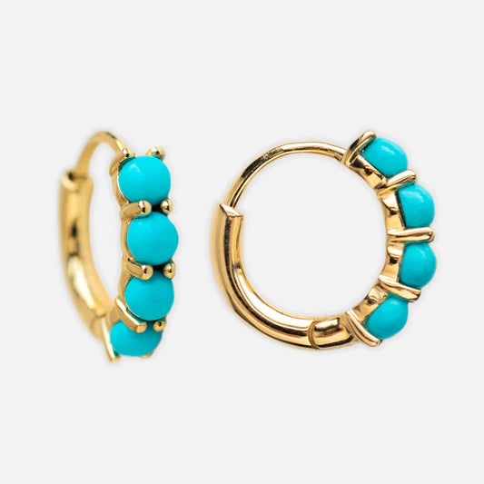 The Solid Gold Turquoise Huggie Hoops feature five round Arizona turquoise stones on each small gold hoop, showcased against a plain white background.