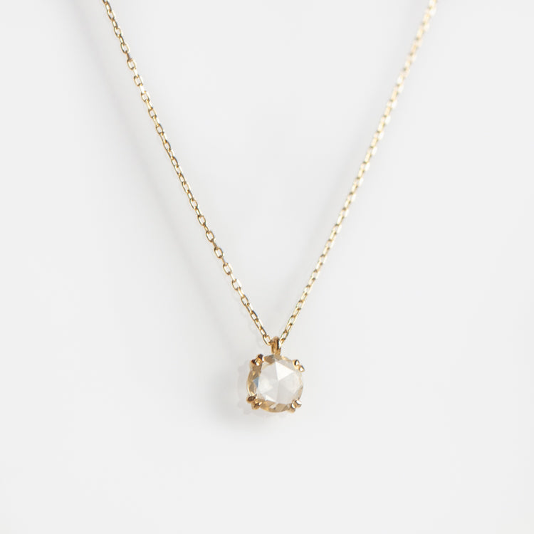 The Solid Gold Shimmering Gemstone Pendant Necklace Sample showcases a round, faceted white sapphire pendant on a delicate yellow gold chain, set against a plain white background.