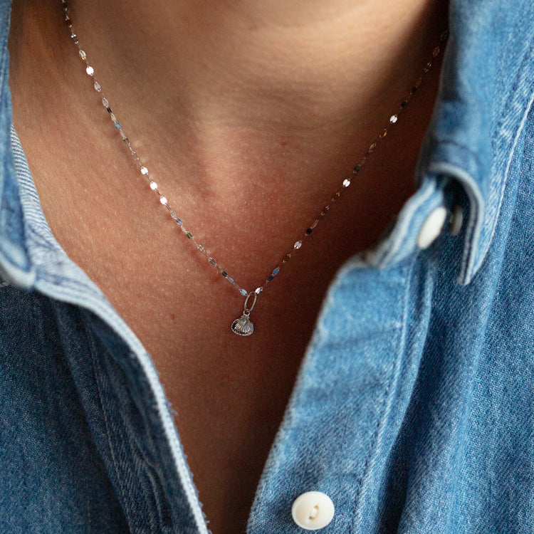 A person wearing a blue denim shirt with white buttons and a delicate Solid Gold Nature Charm in White Gold necklace.