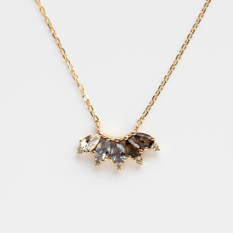 The Solid Gold Ombre Birthstone Necklace June Sample is a 9k yellow gold chain with a fan-shaped pendant, featuring five marquise-cut stones in clear, gray, and brown shades—ideal for those who love distinctive white topaz jewelry.