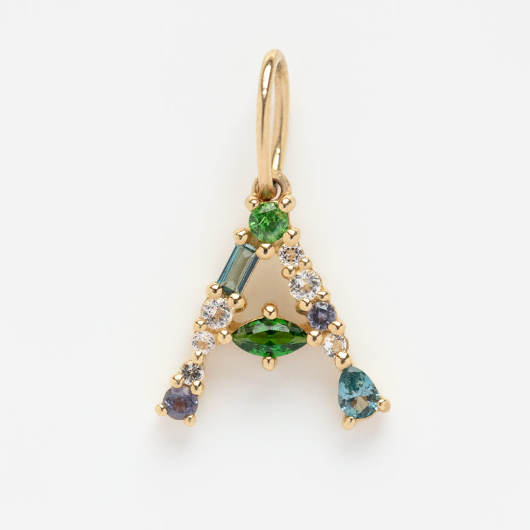The Solid Gold Gemstone Letter Charm is an A-shaped pendant featuring green, blue, clear, and purple stones in various shapes set against a white background for a personalized gold accessory.