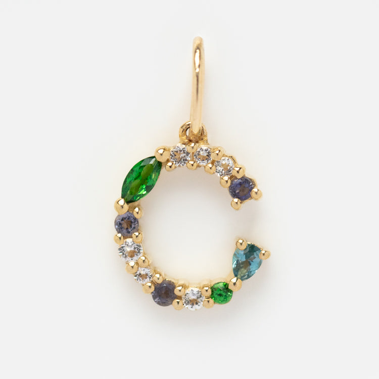 The Solid Gold Gemstone Letter Charm features a gold C shape adorned with alternating green, blue, and clear gemstones, attached to a small gold loop at the top.