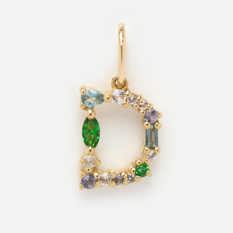 The Solid Gold Gemstone Letter Charm features a gold pendant shaped like the letter D, embellished with blue, green, and clear gemstones in various shapes on a white background.