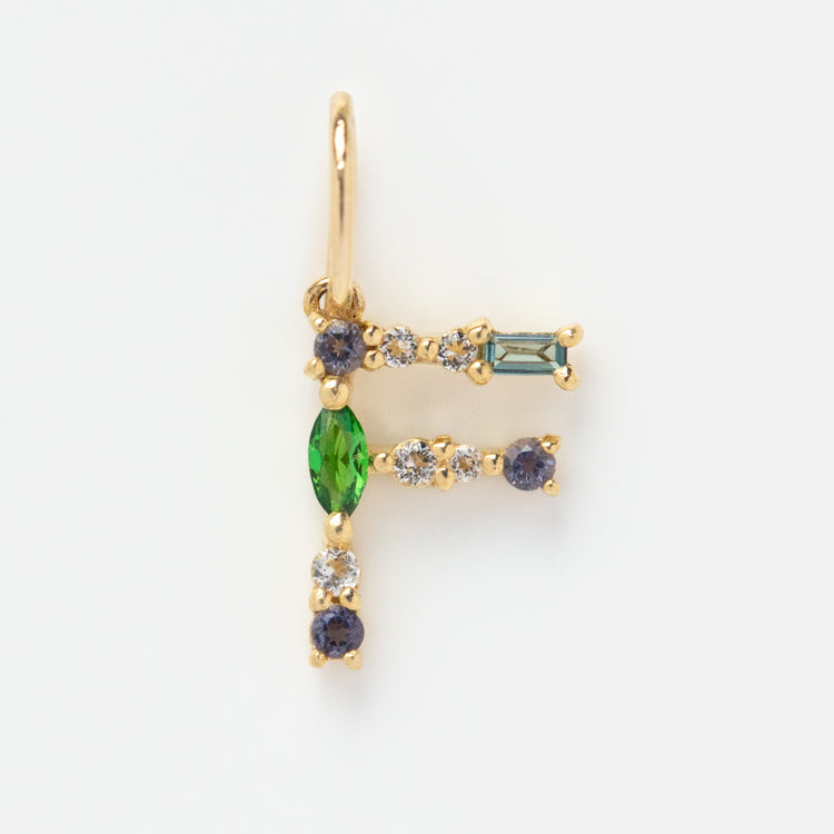 The Solid Gold Gemstone Letter Charm is shaped like the letter F and features small round white, blue, and green gemstones set along its lines for a unique look.