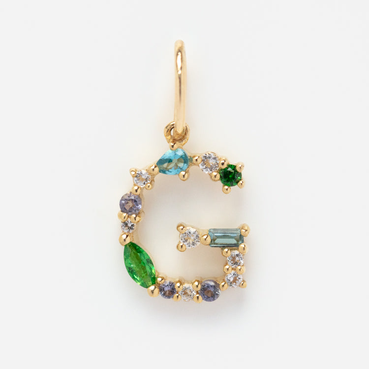The Solid Gold Gemstone Letter Charm features a gold letter G pendant adorned with green, blue, and clear gemstones, displayed on a plain white background.