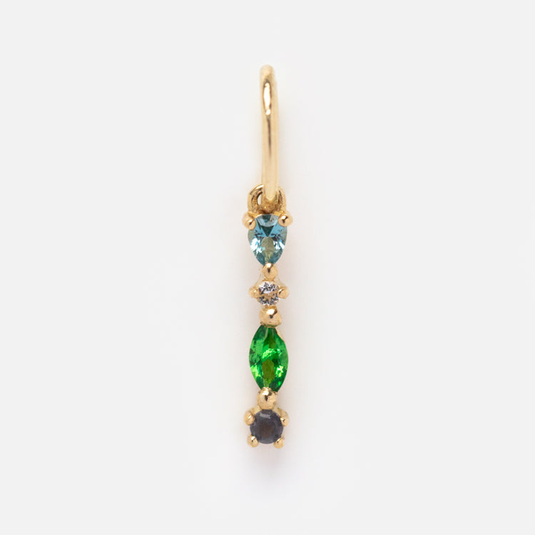 The Solid Gold Gemstone Letter Charm features four vertically aligned gemstones—a light blue teardrop, a small clear round stone, a marquise-shaped green gem, and a round dark blue stone—set on gold against a white background.
