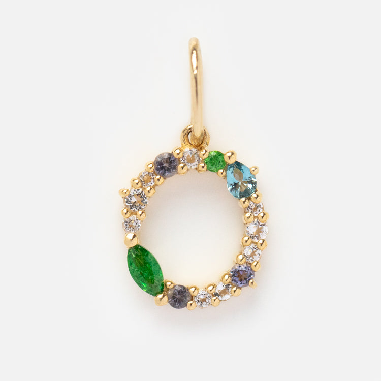 The Solid Gold Gemstone Letter Charm is a small, personalized pendant featuring clear, green, and blue gemstones set in a delicate open circle design.