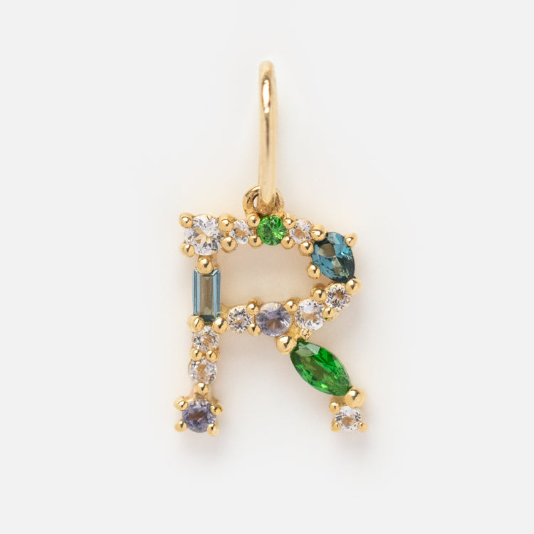 The Solid Gold Gemstone Letter Charm is a gold pendant shaped like the letter R, featuring round, oval, and baguette-cut gemstones in white, green, and blue tones on a plain white background.