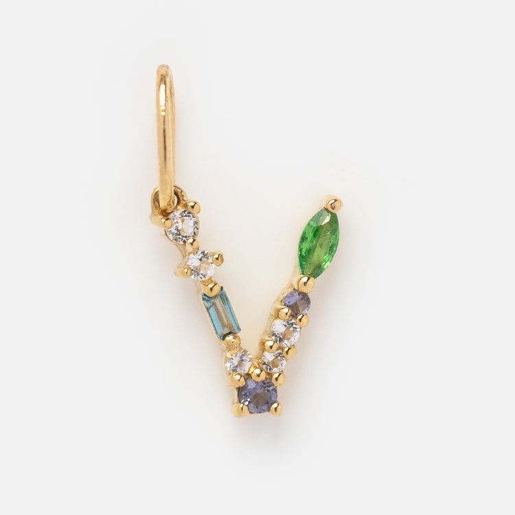 The Solid Gold Gemstone Letter Charm features a V shape adorned with small diamonds, blue stones, and a green marquise-shaped gem, all set in an elegant design.
