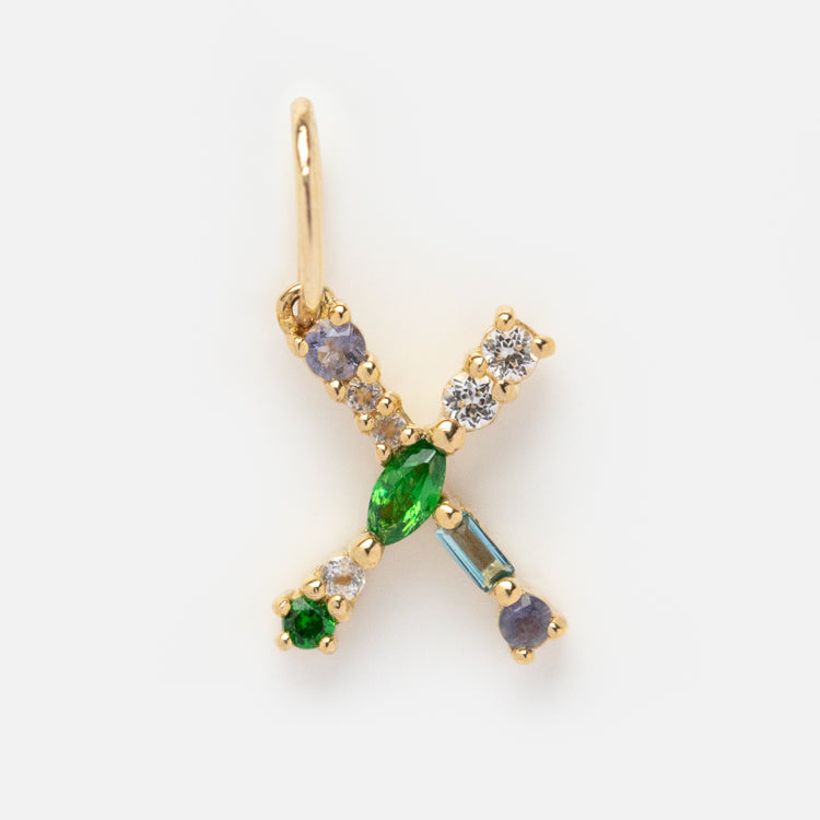 The Solid Gold Gemstone Letter Charm features vibrant gemstones and a small letter x, adding a unique and elegant touch to any collection.