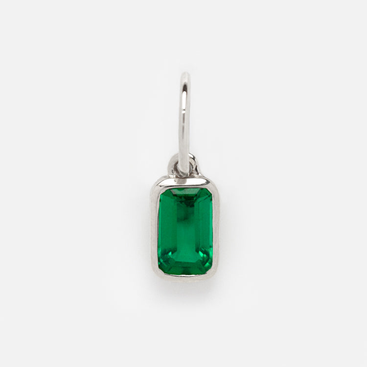 The Solid Gold Birthstone Baguette Charm in White Gold features a rectangular, emerald-green gemstone set in a simple white gold pendant with a small loop for chains, shown on a plain white background.