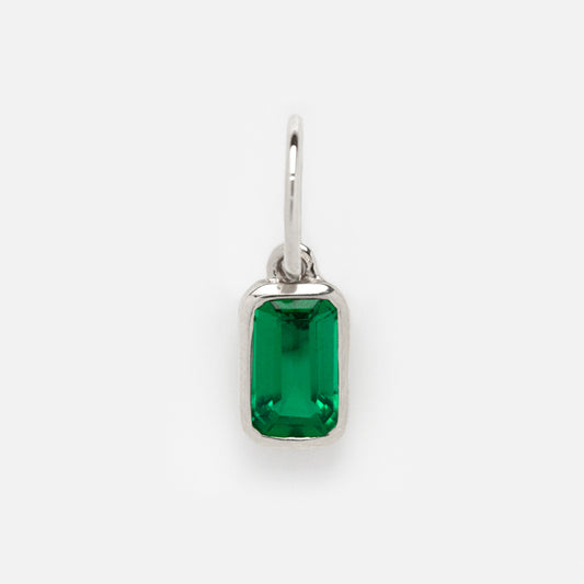 The Solid Gold Birthstone Baguette Charm in White Gold features a rectangular, emerald-green gemstone set in a simple white gold pendant with a small loop for chains, shown on a plain white background.