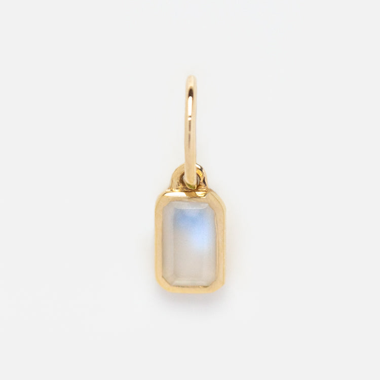 The Solid Gold Birthstone Baguette Charm features a small rectangular iridescent stone set in a gold frame with a loop for attaching to a chain, shown against a white background.