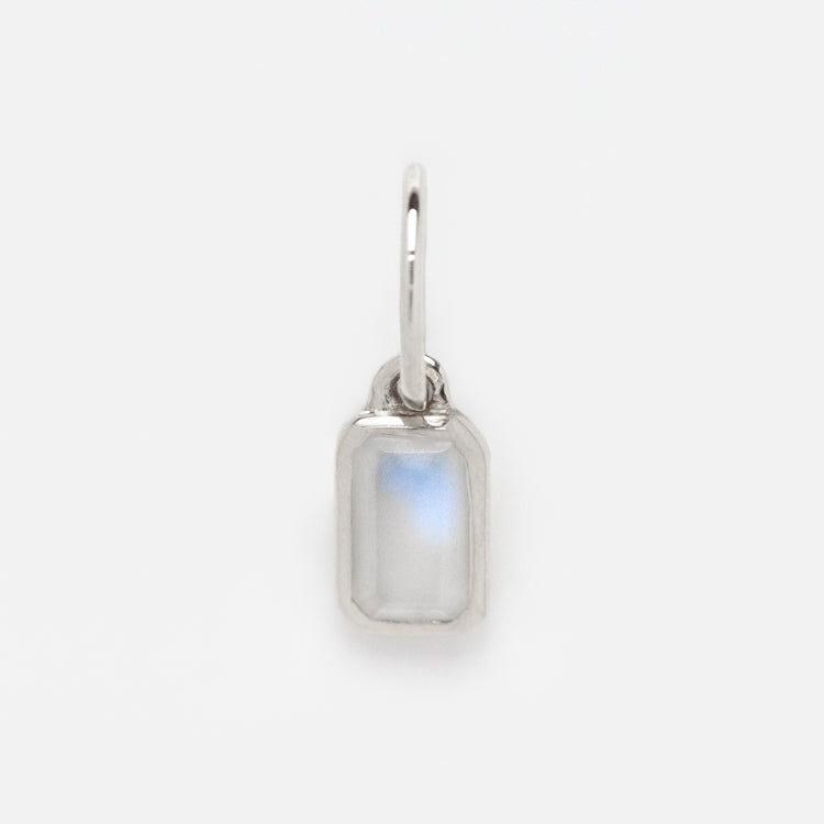 A petite Solid Gold Birthstone Baguette Charm in white gold, showcasing a rectangular translucent gemstone with a subtle blue sheen in a sleek metal frame—an elegant, customizable piece against a plain white background.