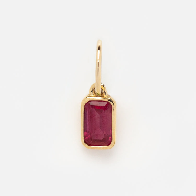 The Solid Gold Birthstone Baguette Charm is a rectangular, faceted red gemstone pendant set in a simple bezel with a small loop—an elegant charm for personalized jewelry, shown on a plain white background.