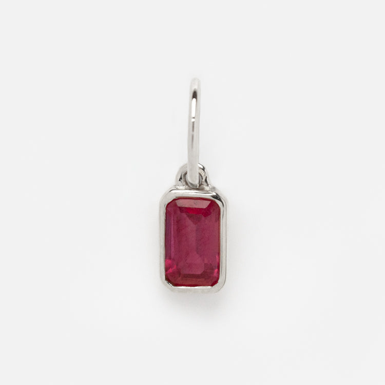 The Solid Gold Birthstone Baguette Charm in White Gold features a rectangular, faceted red gemstone set in a minimalist white gold bezel with a small loop, perfect as a pendant or charm, displayed on a plain white background.