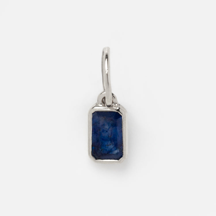 The Solid Gold Birthstone Baguette Charm in White Gold features a rectangular blue gemstone set in a sleek white gold frame, adding personalized elegance to any jewelry collection. Photographed on a plain white background.