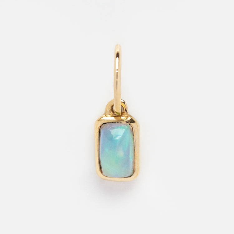 The Solid Gold Birthstone Baguette Charm features a rectangular opal baguette in a gold bezel, hanging from a small hoop and shown on a plain white background—ideal for personalized jewelry collections.