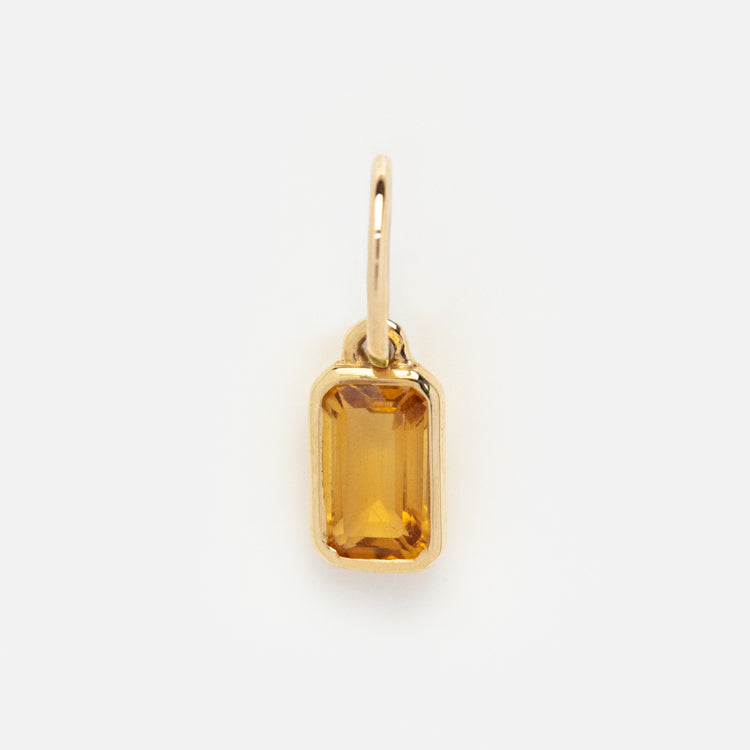 The Solid Gold Birthstone Baguette Charm features a rectangular, faceted yellow-orange gemstone in a simple gold frame with a loop for attaching to a chain—an ideal piece of personalized jewelry.